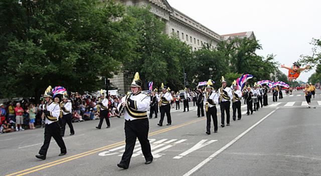 VSHS Band members march down Constitution Ave. July 4; with a giant Fred Flinstone behind them.