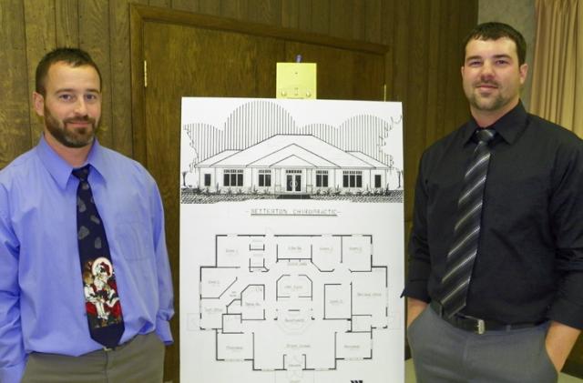 Chiropractors Matt Betterton and Scott Barron stand near a sketch of their new building.