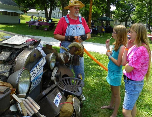 Hillbilly Bob Hill uses a goat to inflate balloons for two girls at Garrison Fun Day Saturday.