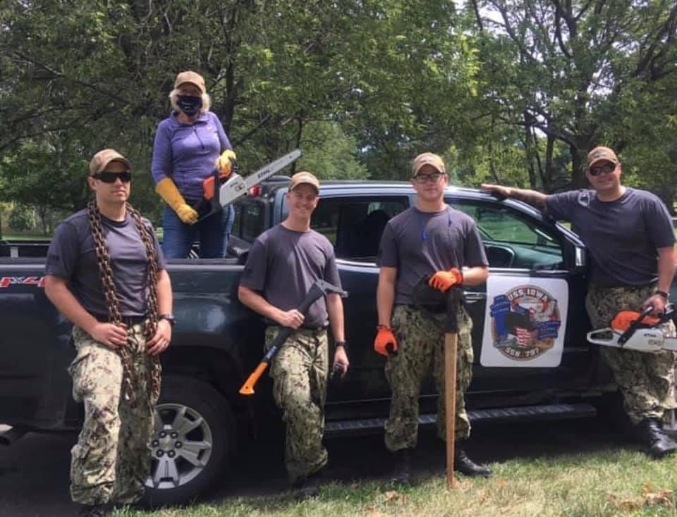 Former Iowa first lady Christie Vilsack, standing in the back of a pickup truck with a chainsaw, and U.S. Navy crew members of the new USS Iowa submarine, are shown here cleaning up grounds of the Iowa Veterans Home in Marshalltown after the August 2020 d