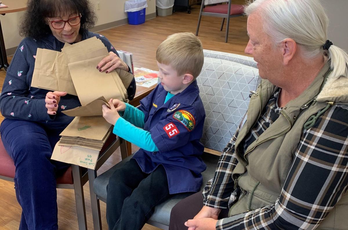 Levi Neuhaus shows Lori Smith and Dawn Stephenson the decorated bags created by Cub Scout Pack 55