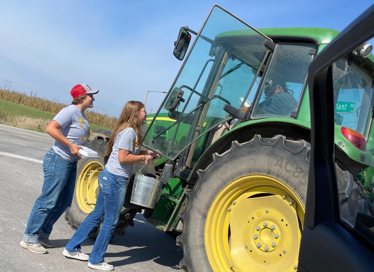 Isabel Mullinex and Bailey Weeks handing a farmer their meal as they met him on the road.