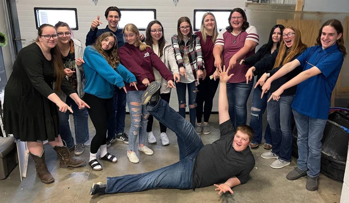 Juliana Luis, Jeana White, Jade Pohlman, Spencer Williams, Alana Fleming, Megan Schlitter, Carlie Clark, Amber Deklotz, Kylee Kirchner, Gracie Fish, Izzie Birker, and Brody Waters point at Andrew Pingenot as they all pose for a group photo.