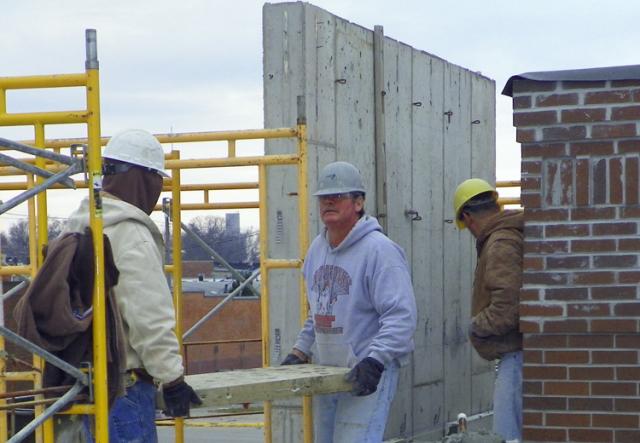 Workers carry a limestone block to place it on south side of LEC, facing courthouse.