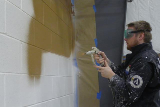 Maple 4 Corps Member John MacKinnon sprays paint onto the walls of the new Northeast Iowa Food Bank