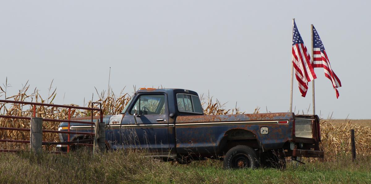 An old pickup, parked near a field of corn, flying two flags in remembrance of those who lost their lives 20 years ago on 9/11