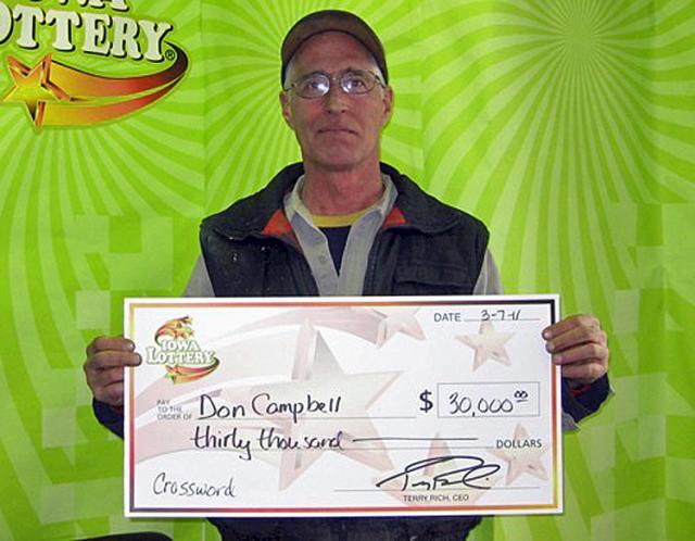 Don Campbell holds Iowa Lottery check after winning $30,000; he bought ticket at John's Qwik Stop.