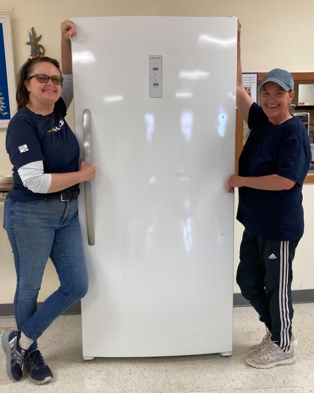 Tricia Hanover and Laurie Spalding are standing next to the new freezer that was generously purchased from Barnes Furniture
