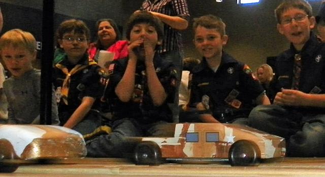 Scouts watch as Pinewood Derby cars race toward the finish line.