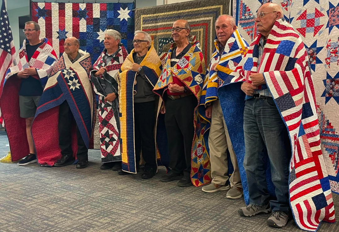 Article Thumbnail. Quilts of Valor presented area Veterans with their very own quilt thanking them for their service. In the very center is Jim Schulte, 2nd from right, Bill Newton.
