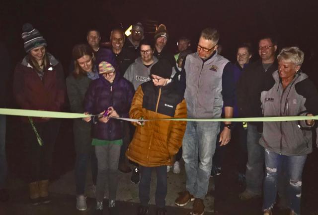 Ashley Hesson holds the ribbon for children Lily and Noah as they perform the ribbon cutting for Nathan's Smiles Trail