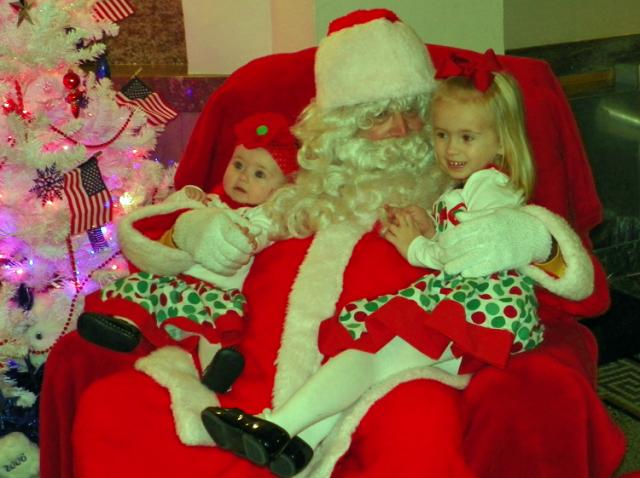 Sophie and Chloe Mossman sit on Santa's lap after his arrival at the courthouse Thursday evening.
