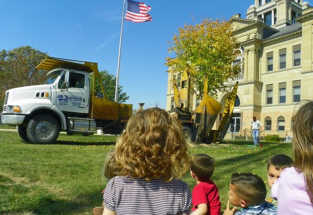 Children watch as the large machine lowers a maple tree into its new place near the courthouse.