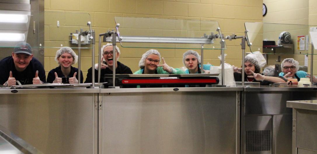 Members Will McKenna, Kirsten Pettit, Bri Dulin, Abby McKenna, Addi Obadal, Aden Dawson-Fink, and Zane Helter pose in between serving meals.