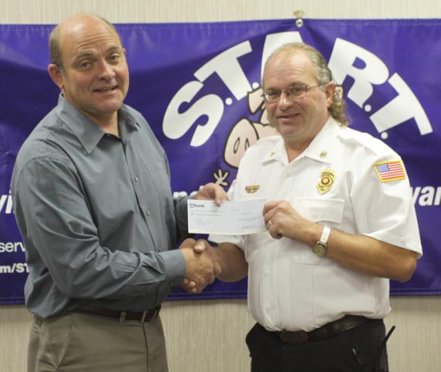 Jon Kremer presents a $2,500 check to Garrison Fire Chief Steve Meyer to assist with storm recovery